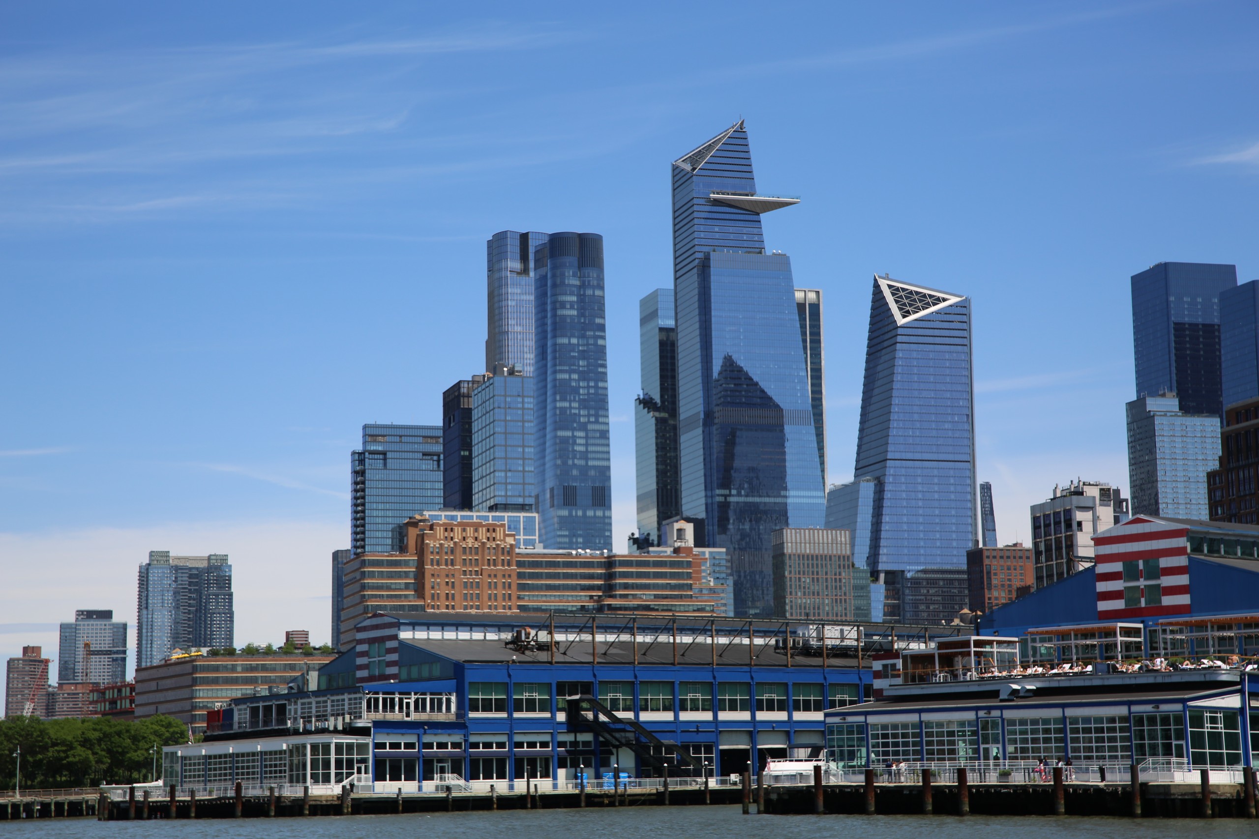 Skyline view of modern skyscrapers with angular designs and a waterfront in the foreground.