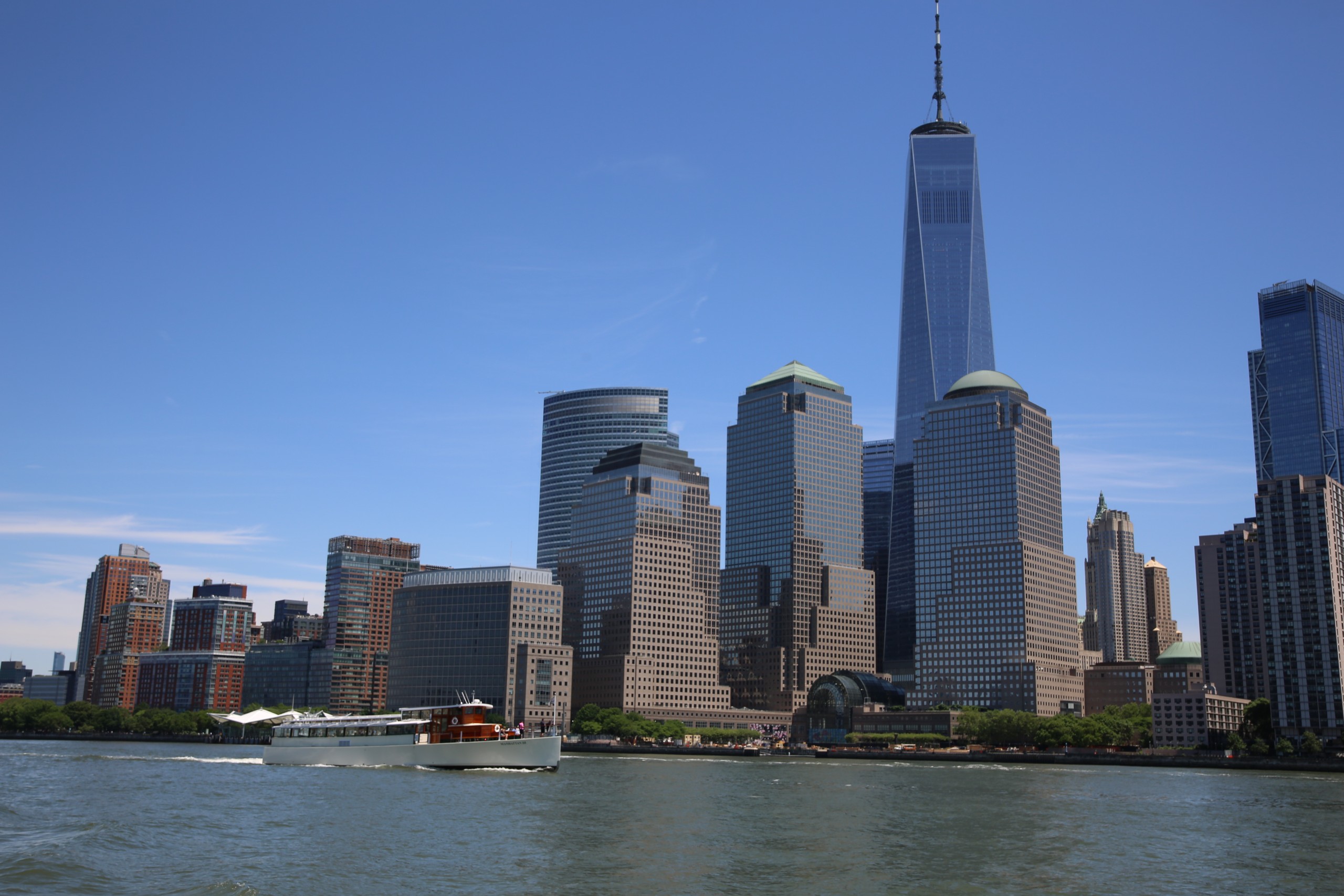 Skyline with tall buildings and a boat on the water under a clear blue sky.