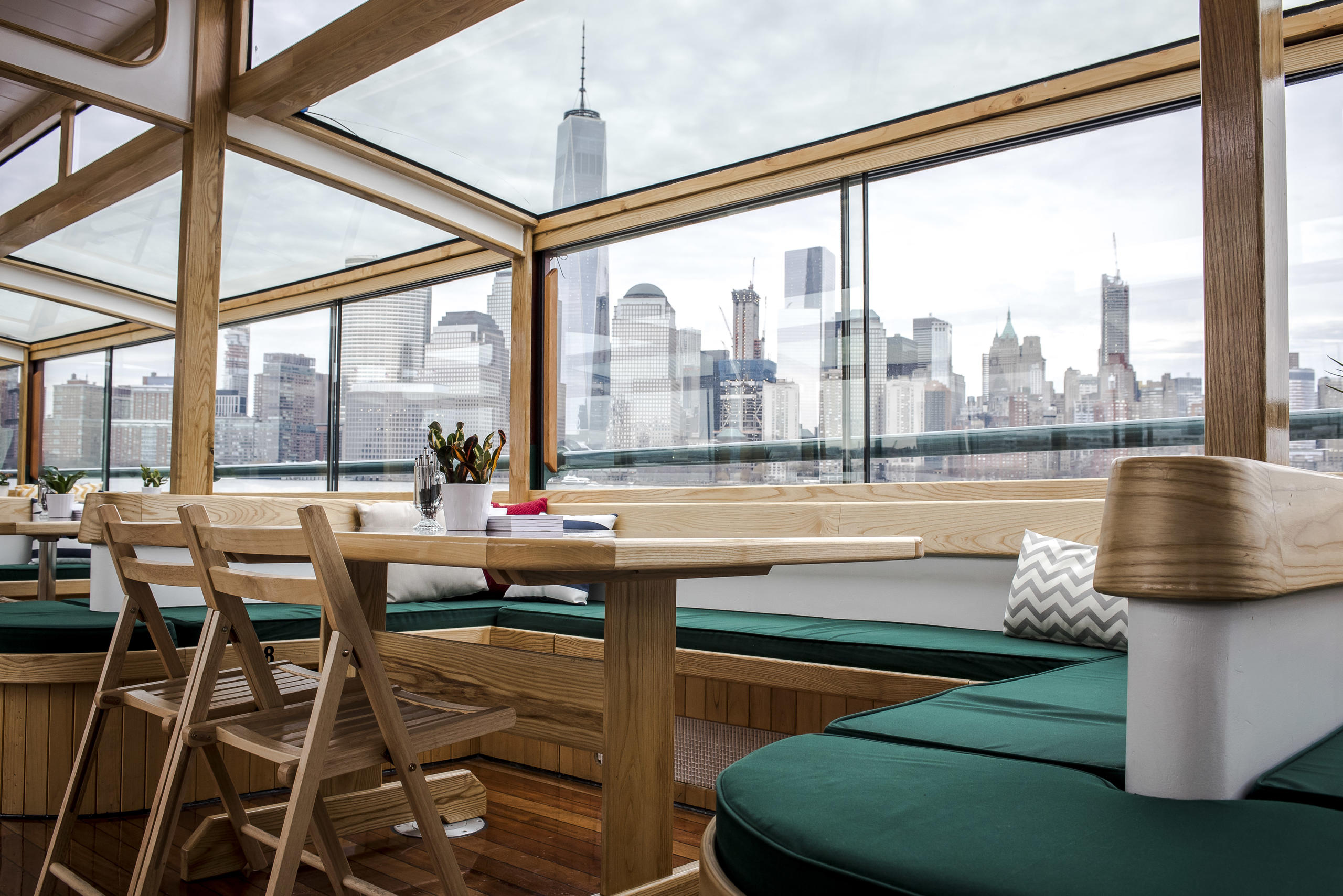 Modern glass-walled interior with wooden furniture overlooking a city skyline.