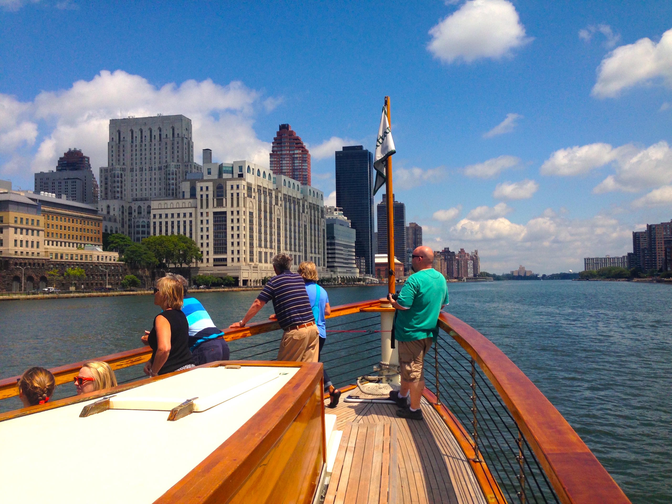 People on a boat deck overlooking urban skyline and river.