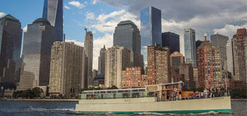 Boat on river with skyscrapers in background under partly cloudy sky.