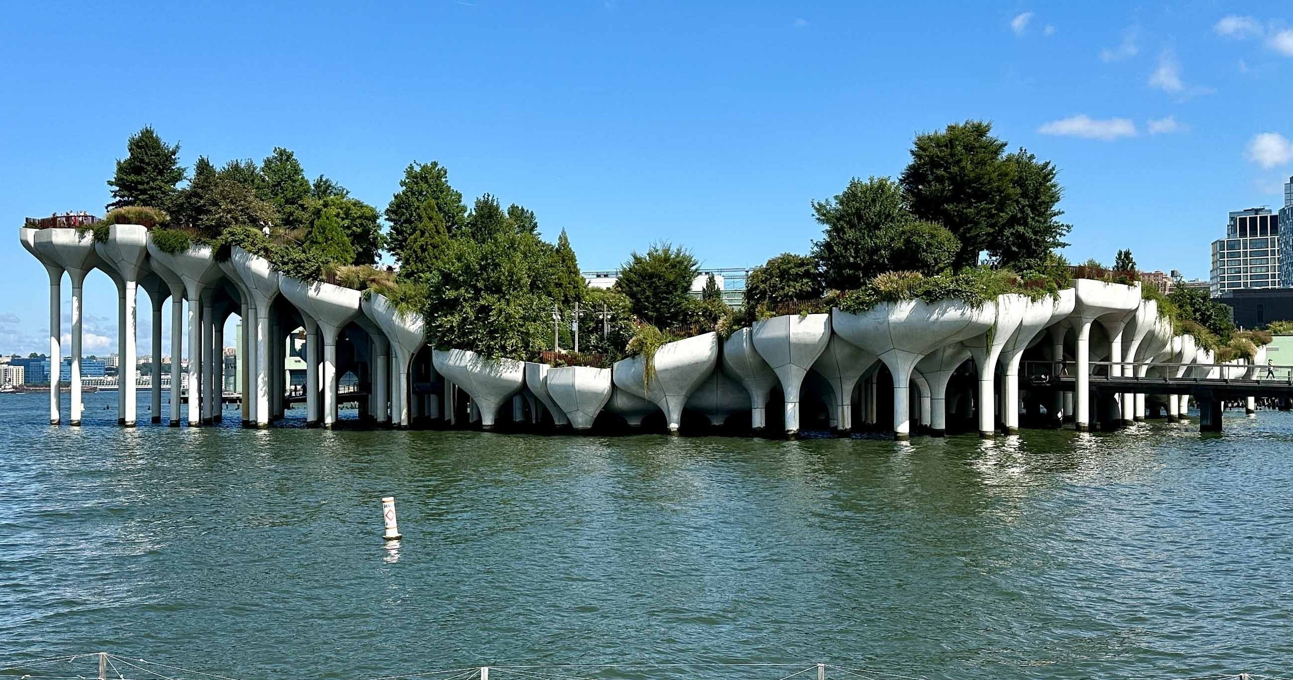 Island park with trees and columns above water on a sunny day.