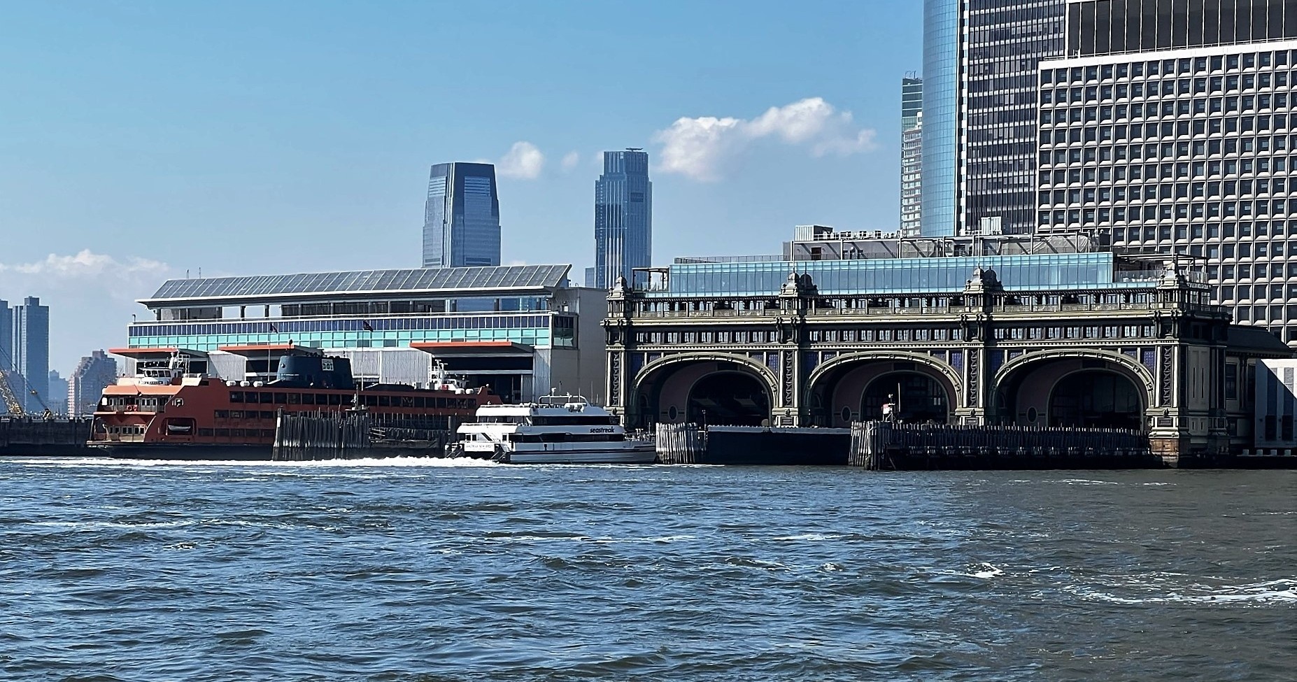 Ferry terminal with buildings, boats, and city skyline on a sunny day.