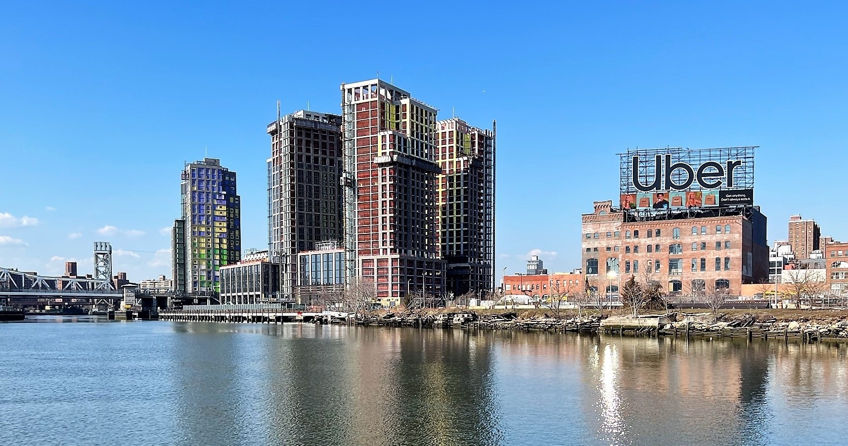 City skyline with tall buildings and a river, Uber sign on a rooftop.