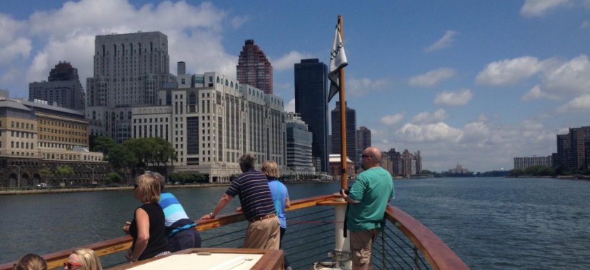 People on a boat deck with city skyline and river view.