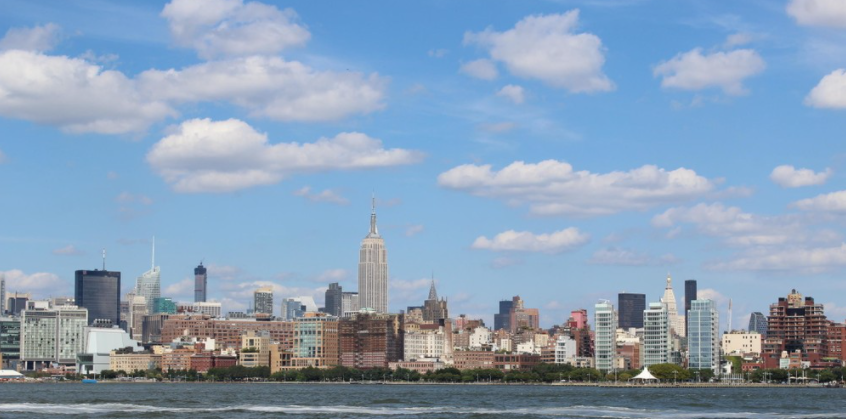 City skyline with skyscrapers under a partly cloudy blue sky.