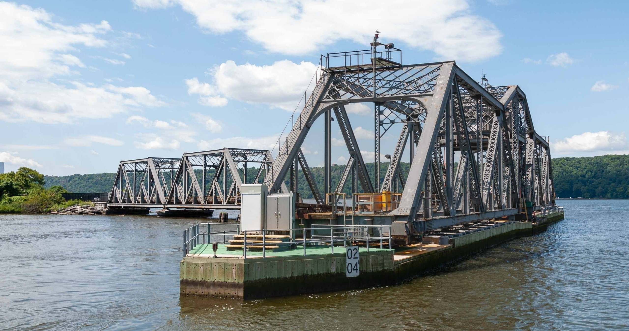 Two steel truss bridges over a wide river under a partly cloudy sky.