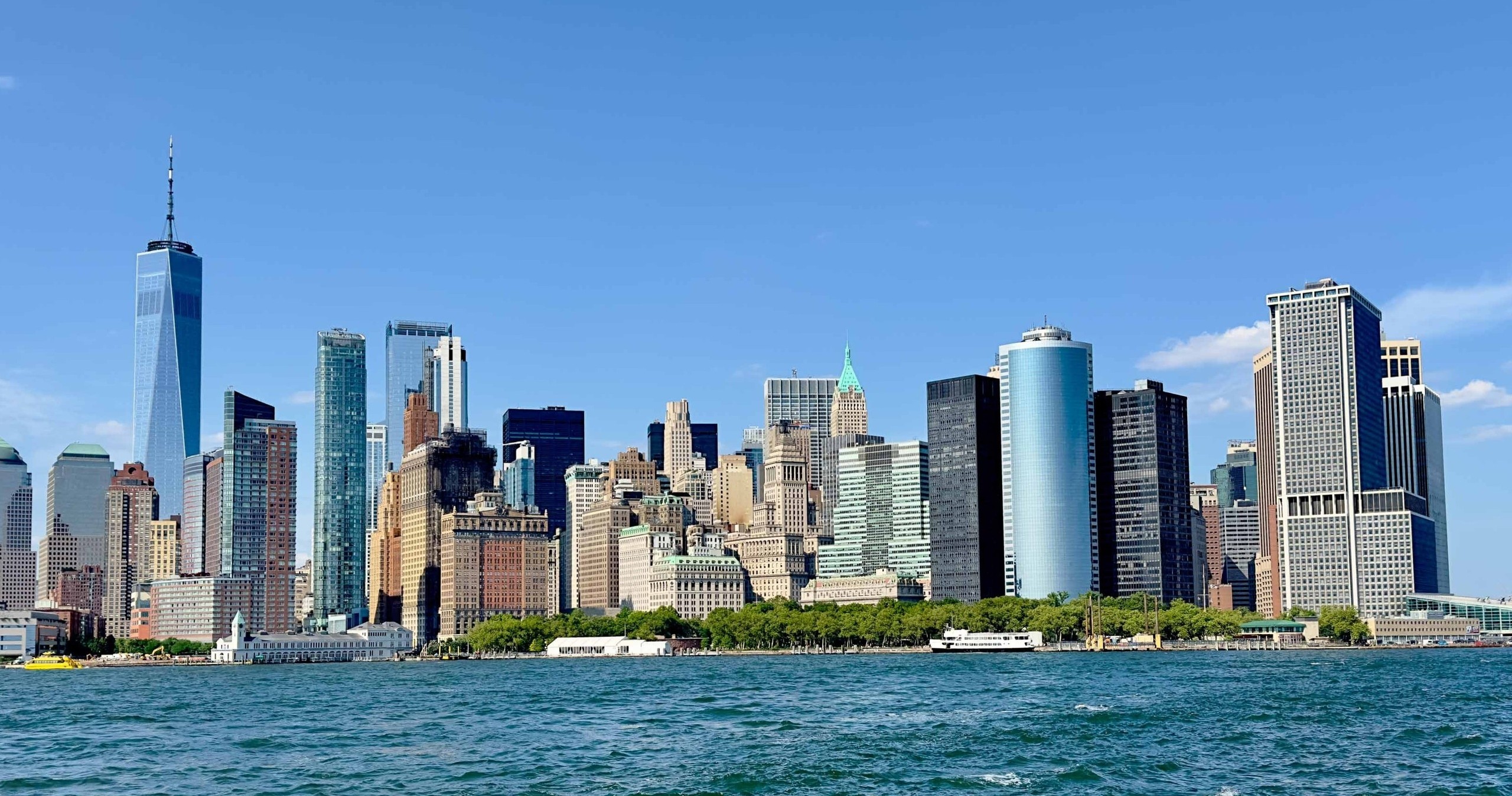 Panoramic view of a city skyline with tall buildings against a clear blue sky above water.