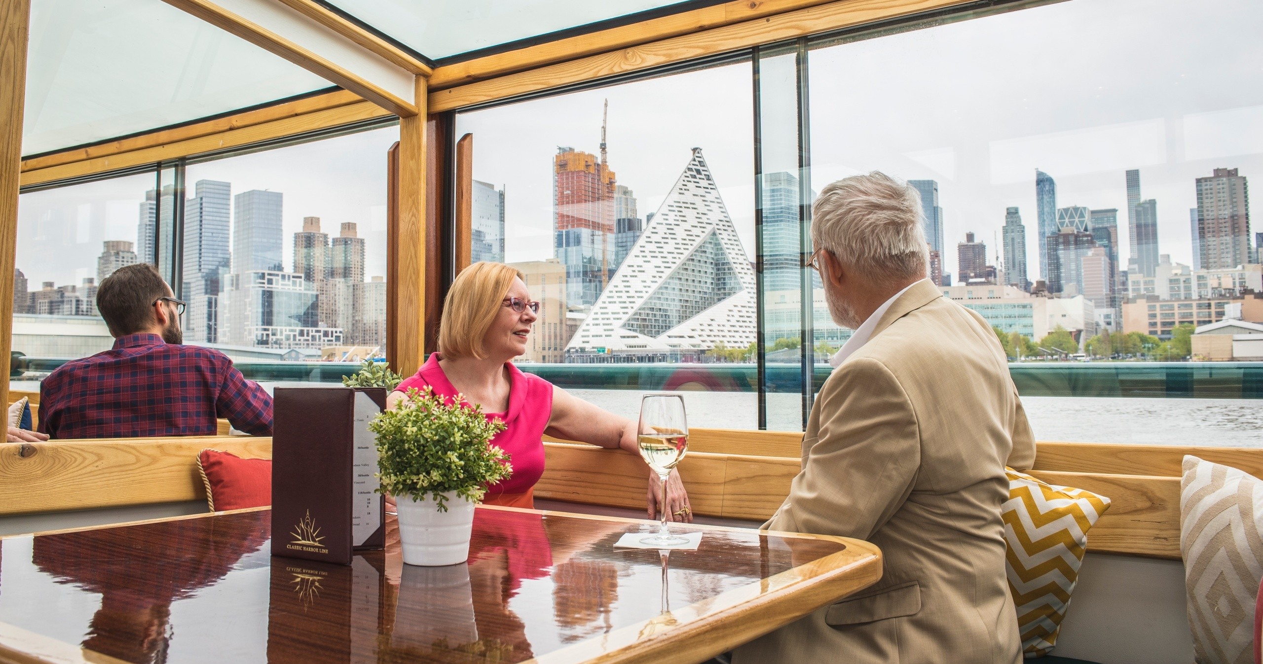 People enjoying drinks on a boat with city skyline view through windows.