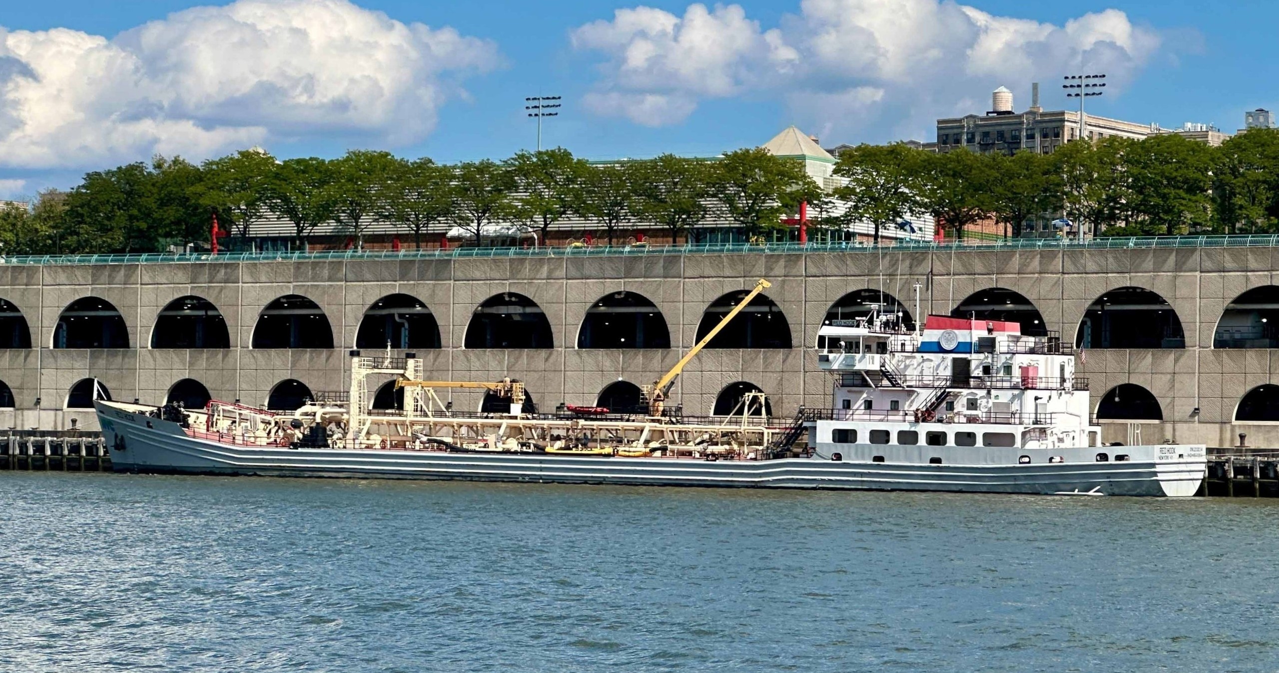 Large ship docked by a waterfront building under a blue sky.