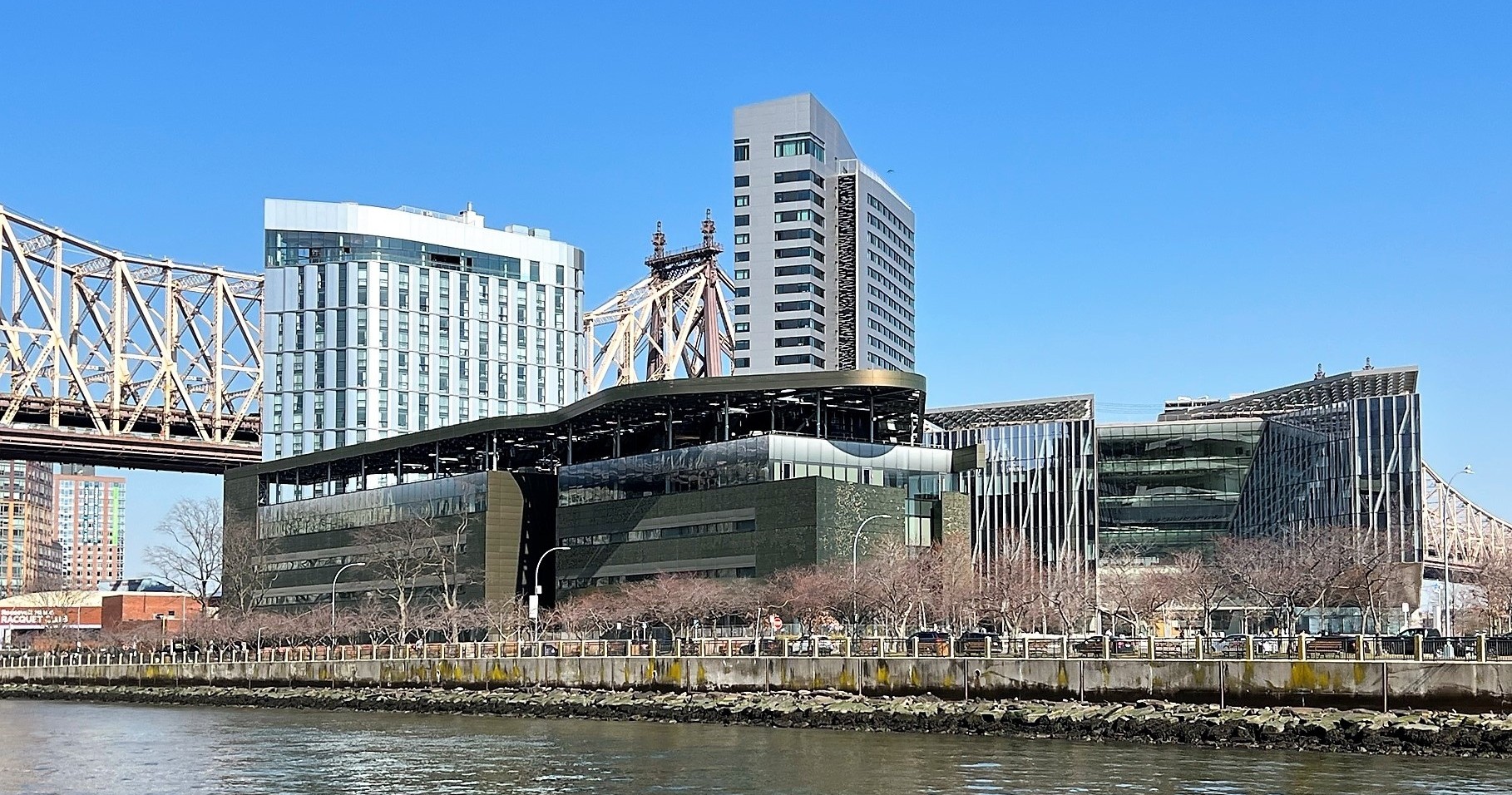 Modern campus buildings near a bridge and river, clear blue sky.