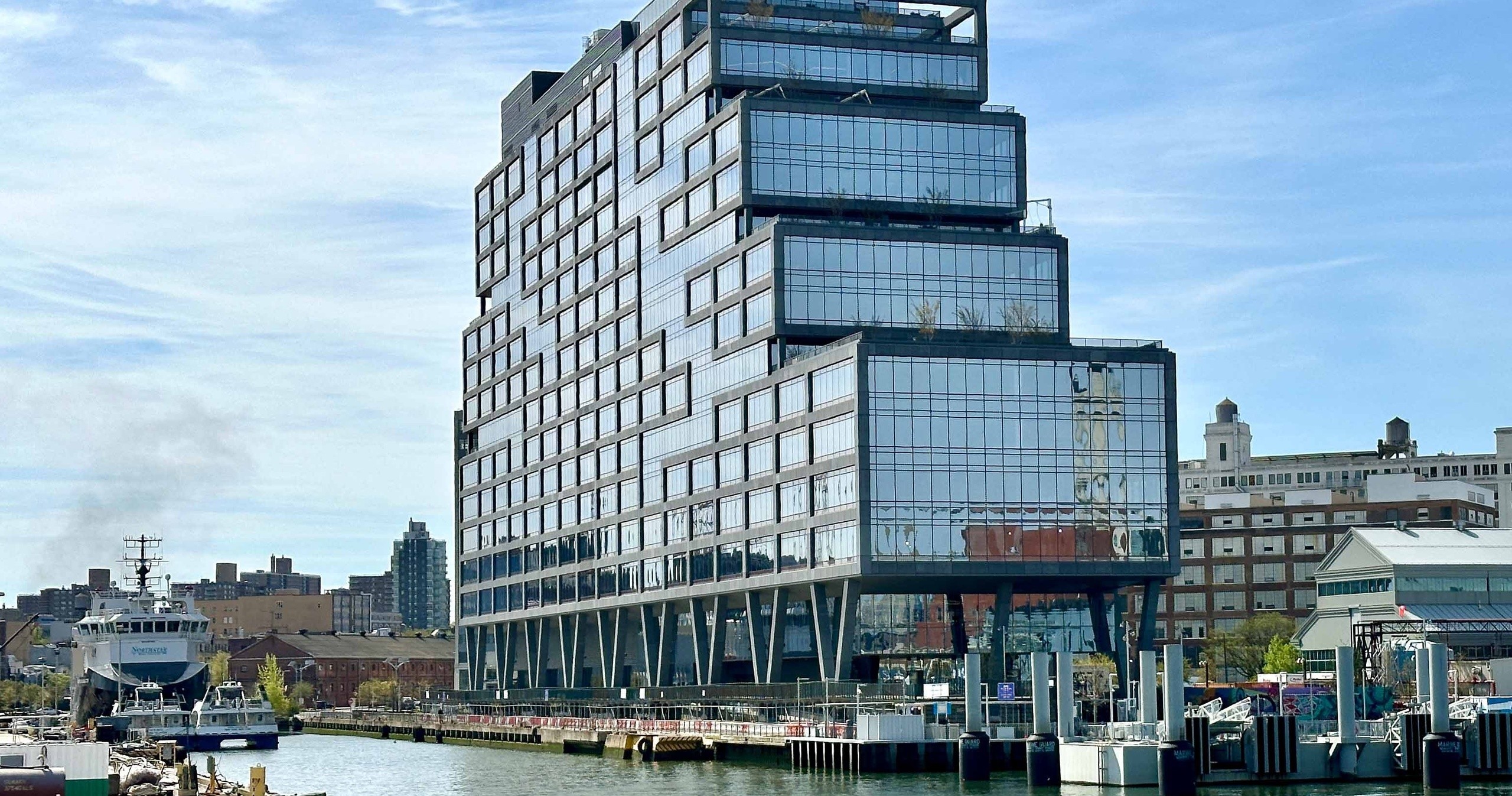 Modern tiered glass building by waterfront with boats and docks.