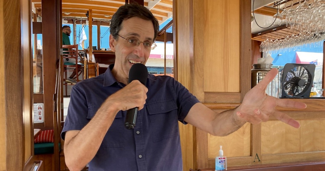 Man speaking into a microphone inside a wooden boat cabin.