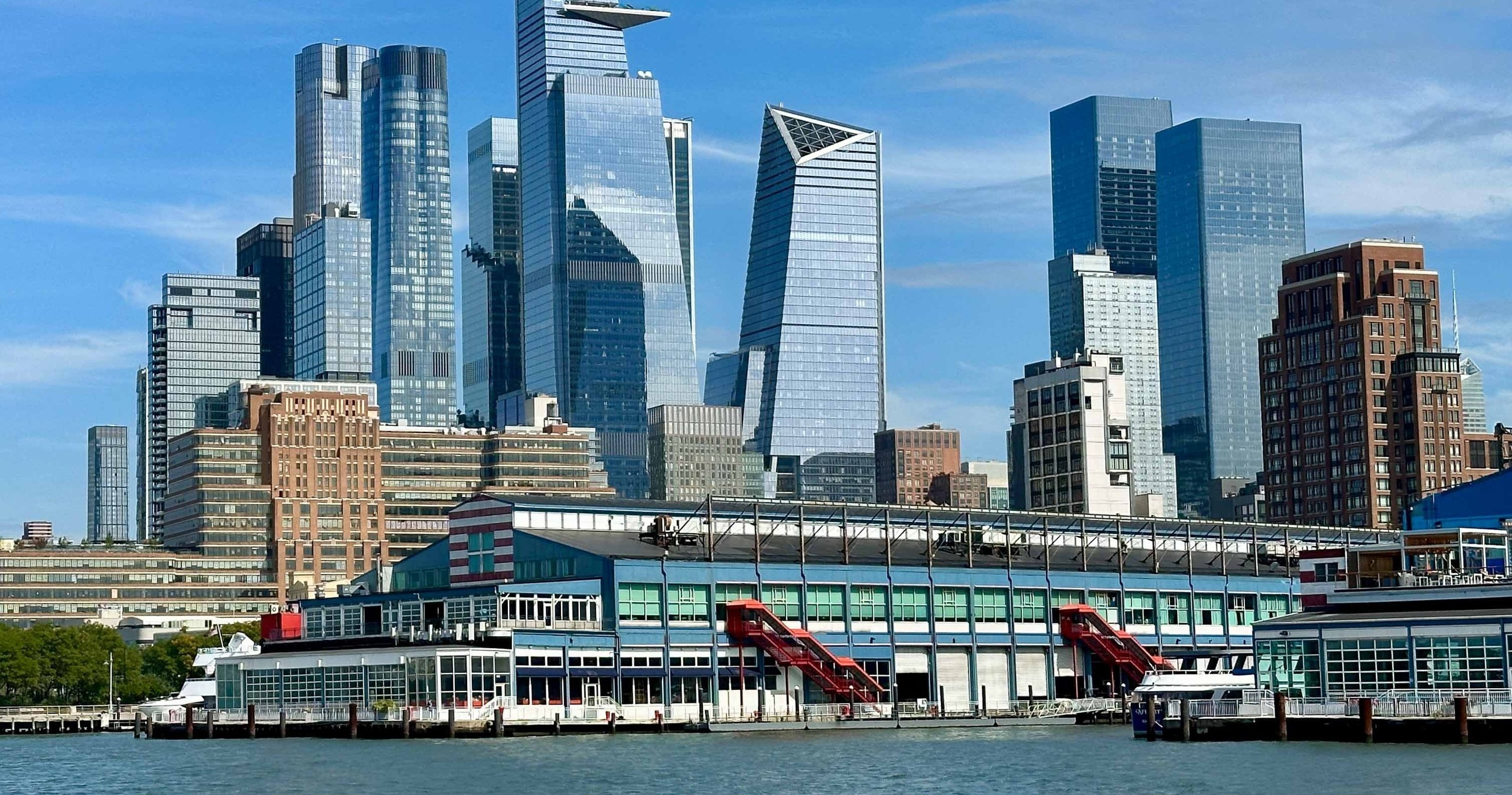 Skyline of modern skyscrapers behind a waterfront pier, under a blue sky.