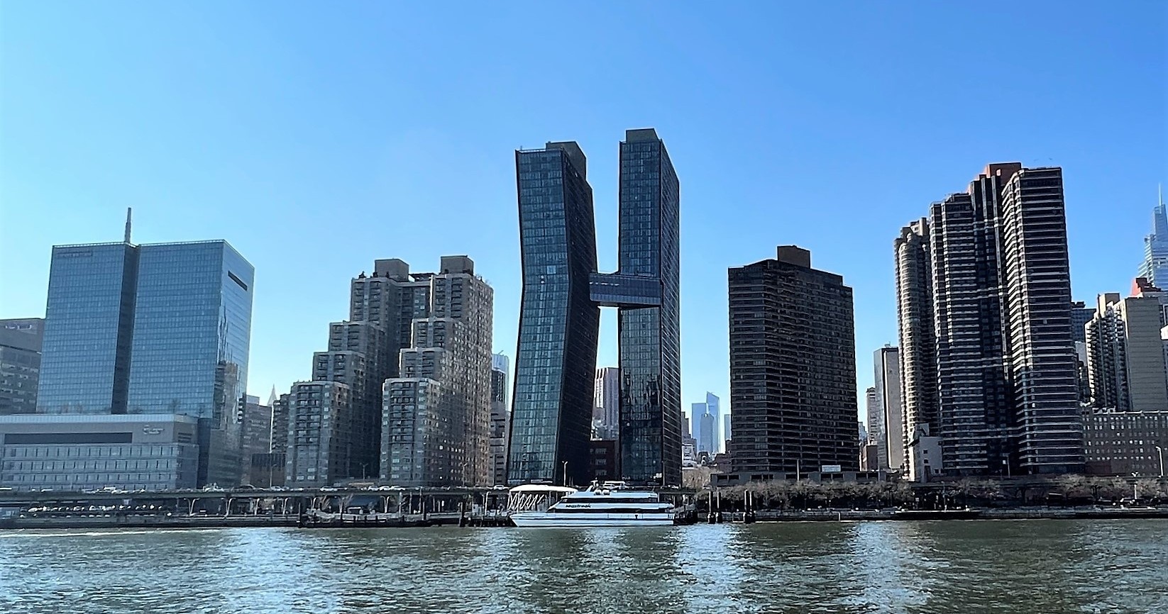 Riverfront cityscape with modern skyscrapers under clear blue sky.
