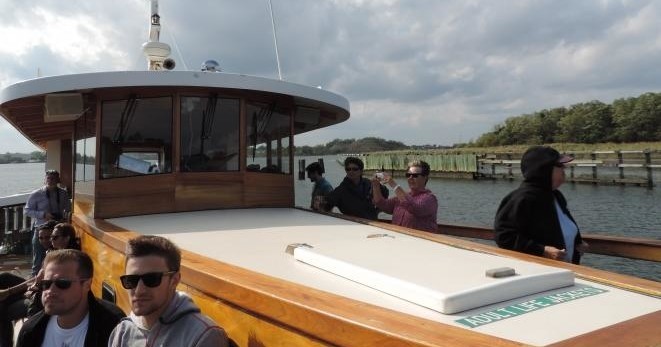 People on a wooden boat docked by a river, with trees in the background.