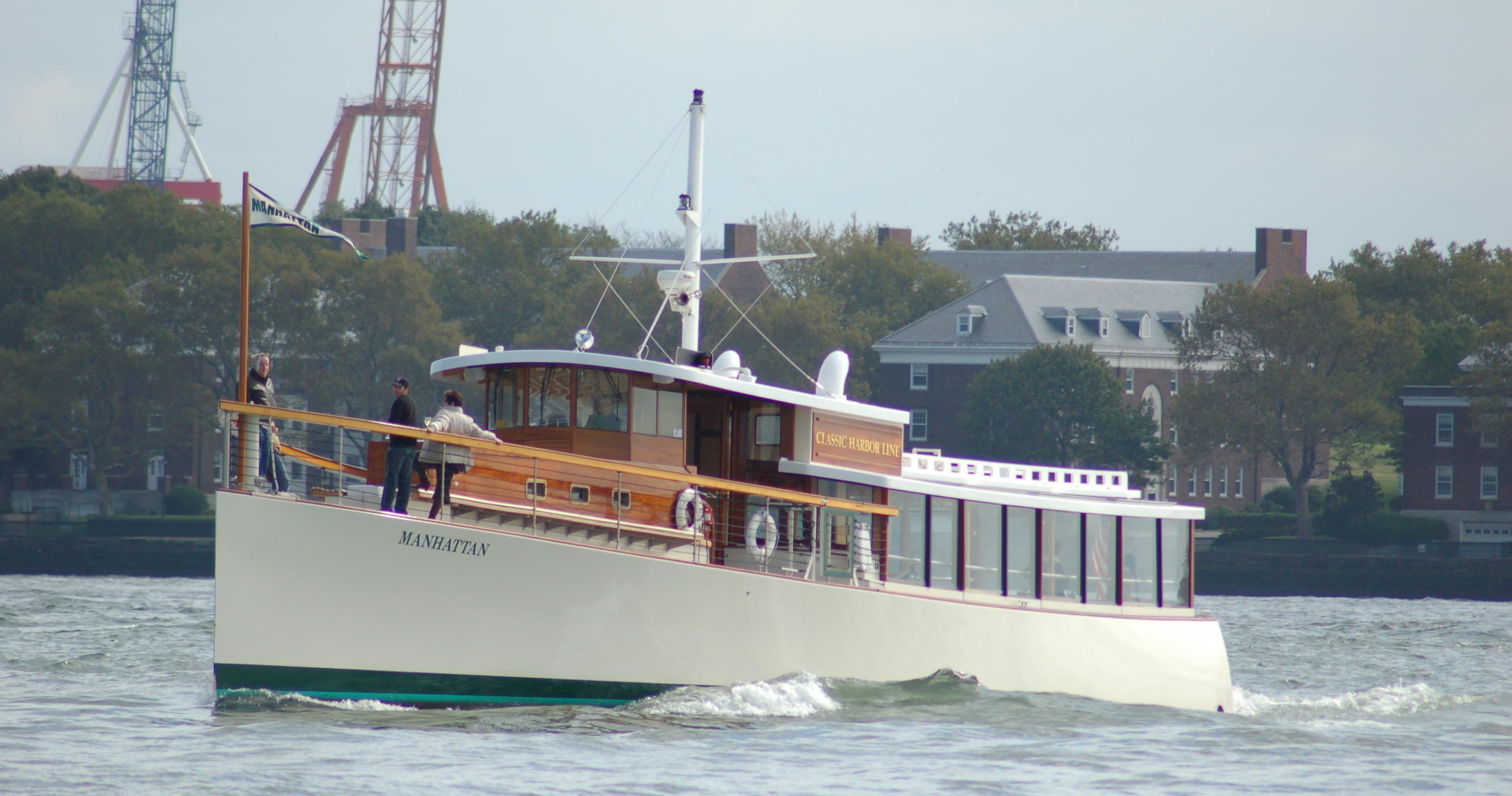 White and wood-trimmed boat with people on deck, cruising on water.