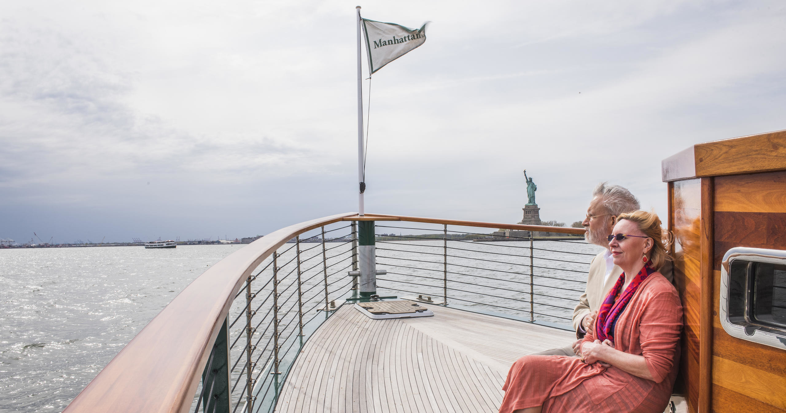Couple sitting on a boat deck with the Statue of Liberty in the background.