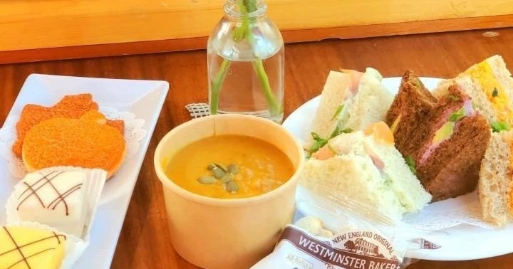 A table with sandwiches, soup, cookies, and a small vase with flowers.