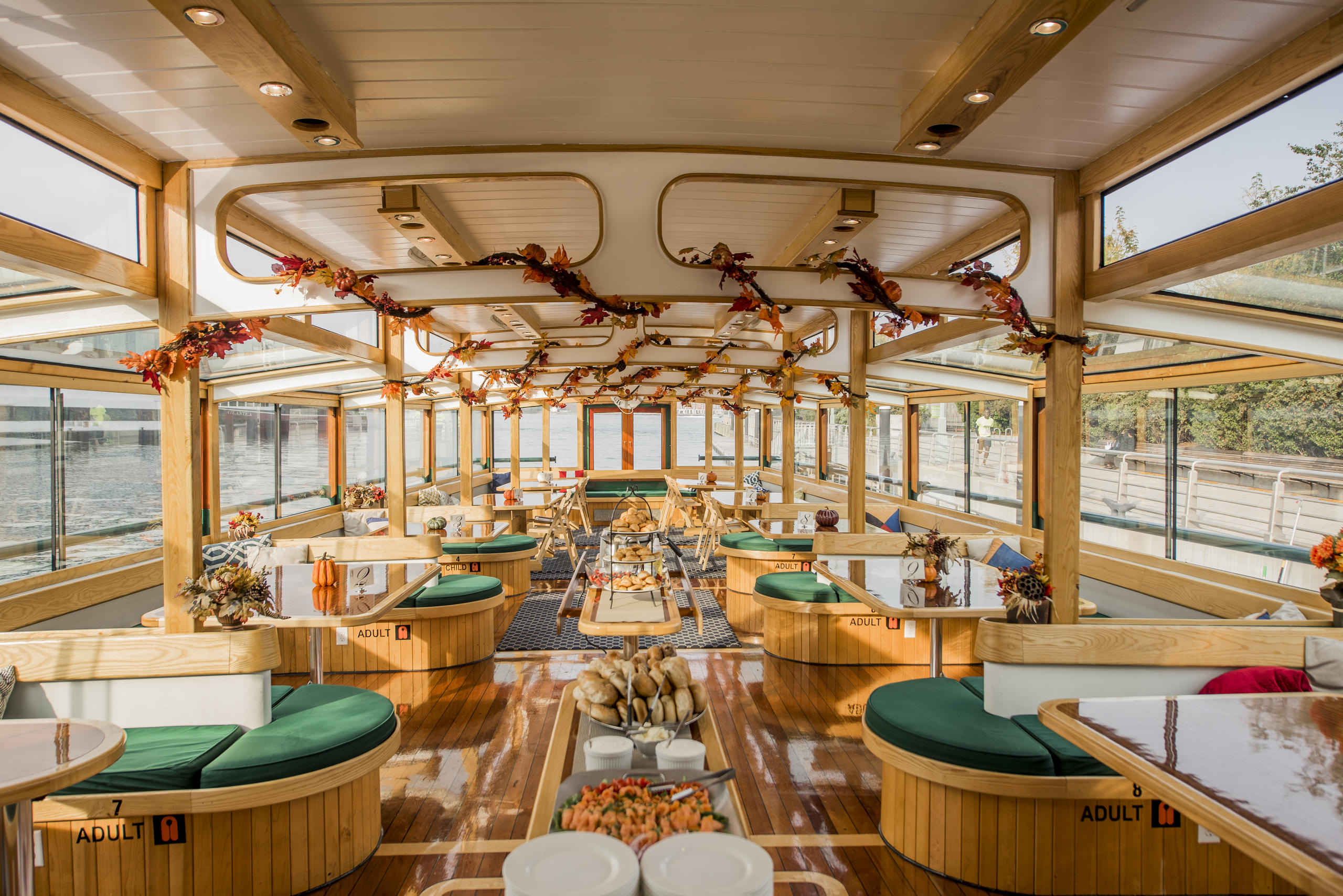Spacious boat interior with wooden décor, round tables, and decorative ceiling garlands.