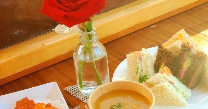 Tea sandwiches, soup, and a red rose on a table.