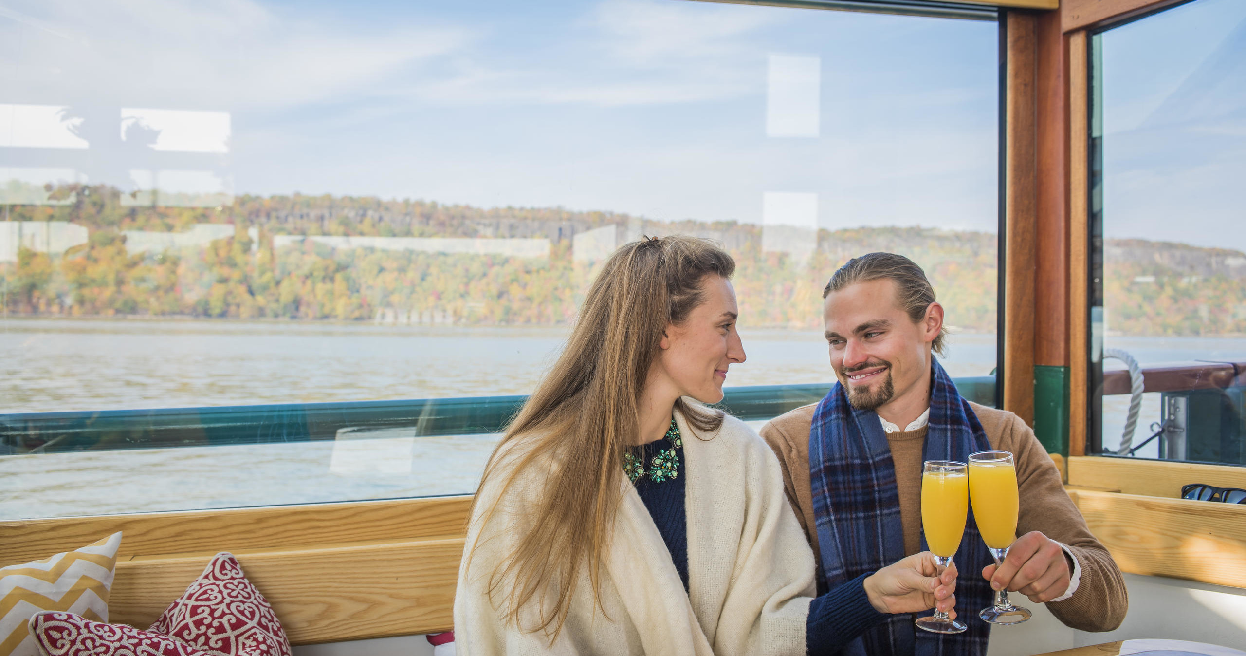 Couple toasting with orange drinks on a boat, scenic view outside.