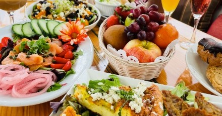 Assorted brunch dishes with salad, fruit basket, and pastries on a table.