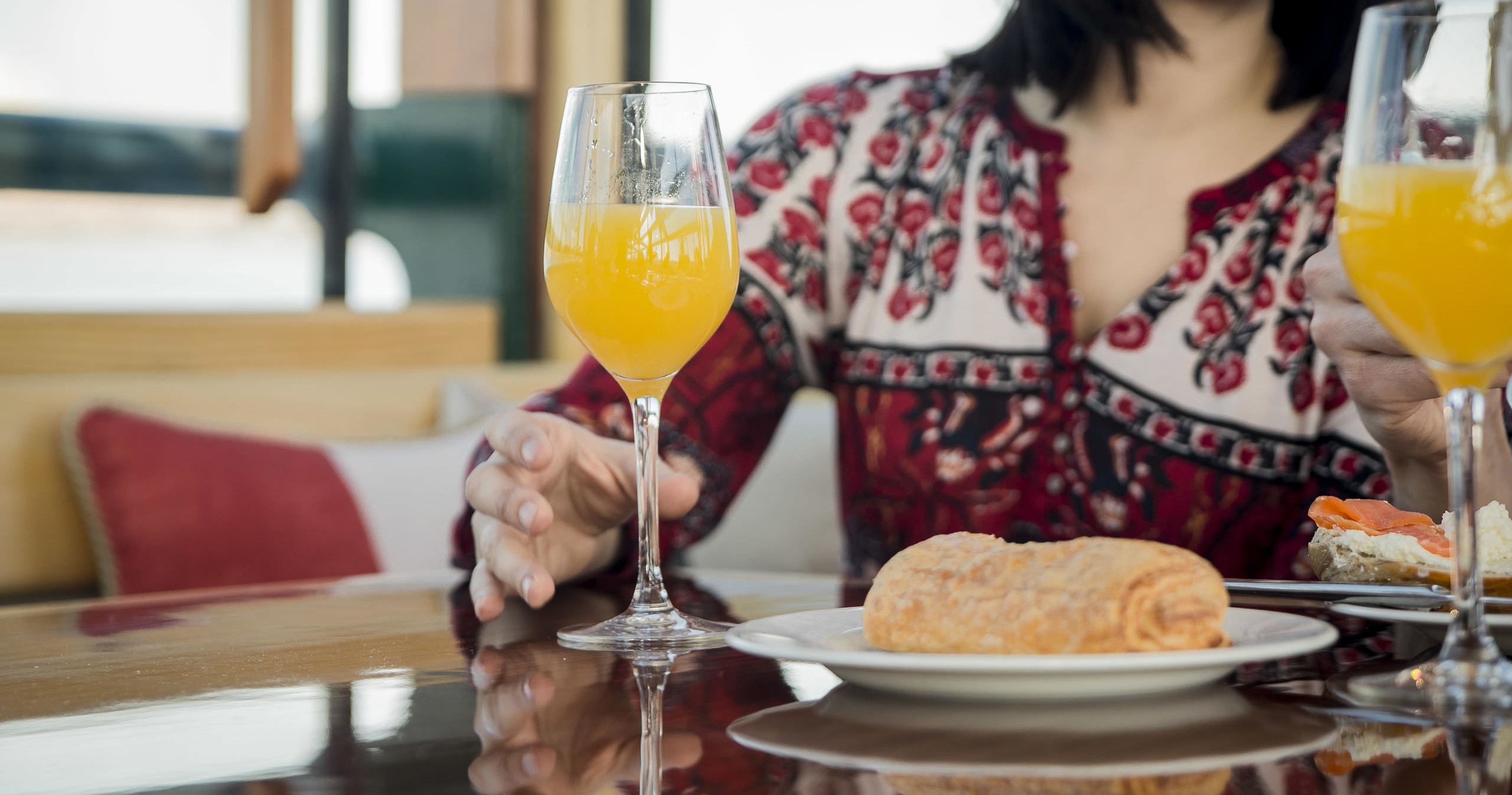 Person in floral shirt with mimosa and pastry on a table.