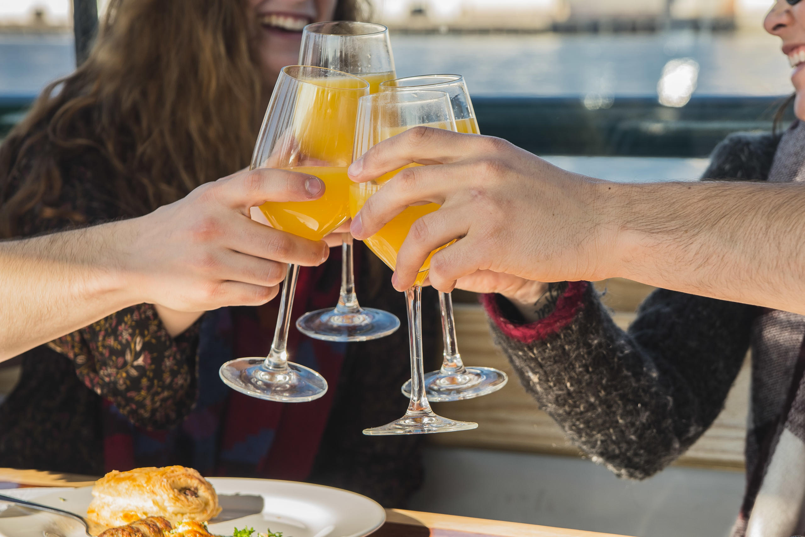 Three people toasting with orange juice in wine glasses.