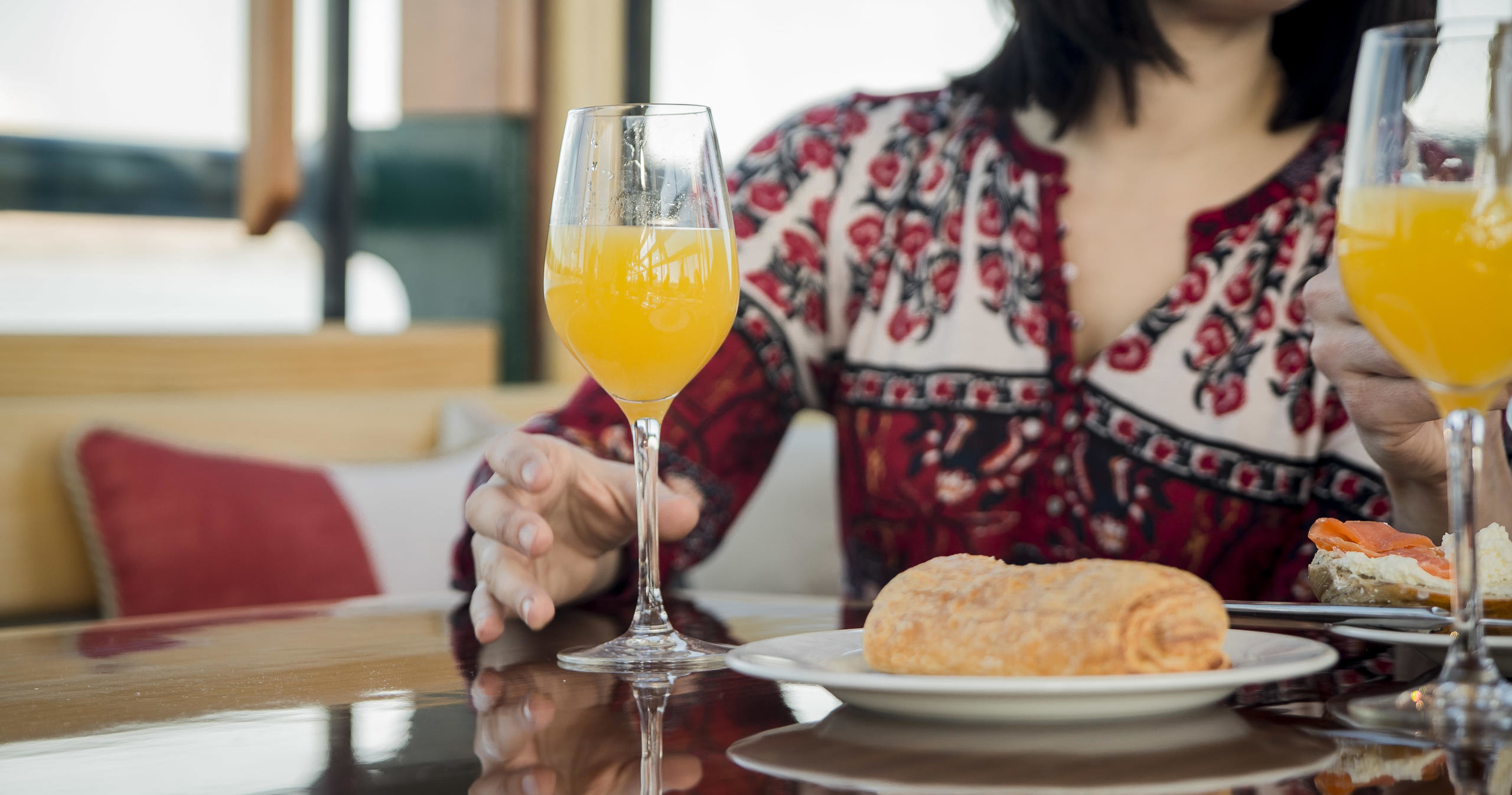 Woman sitting with mimosa and pastry on a table.