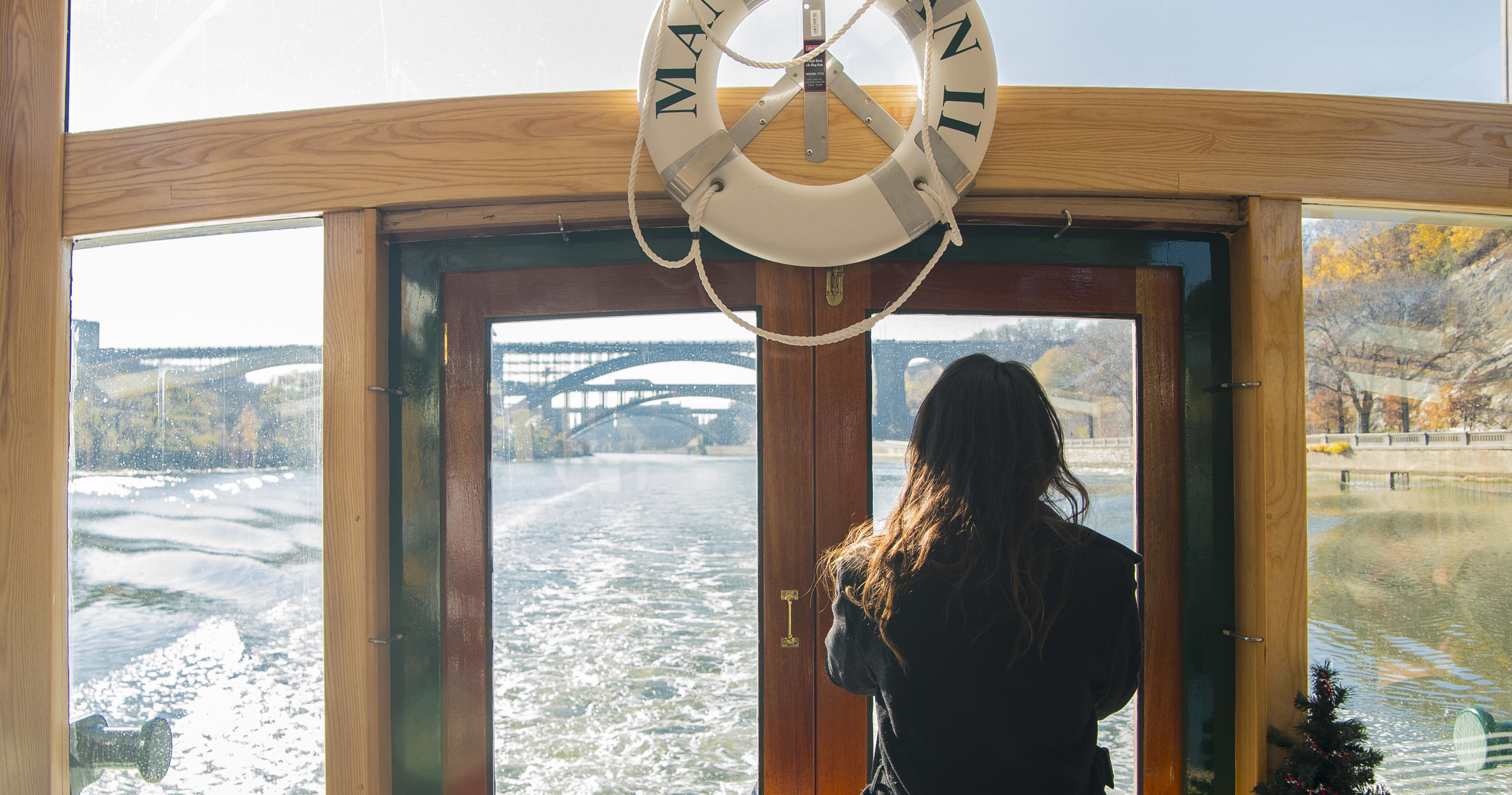 Person on boat looking out at river and bridges in the distance.