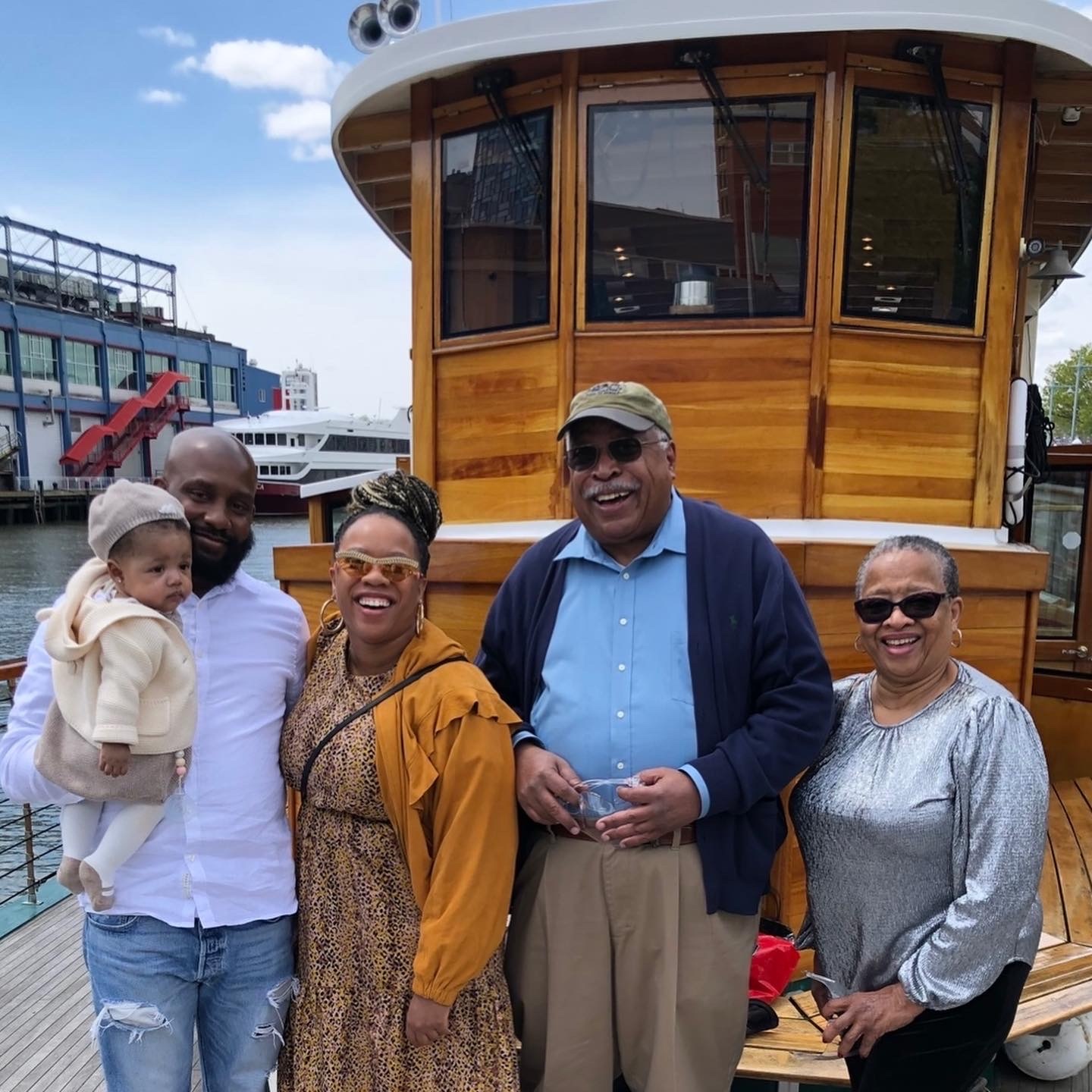 Group of five adults and a baby smiling on a boat dock.