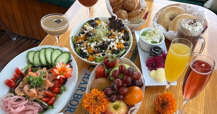 Brunch spread with salads, bagels, fruits, and drinks on a wooden table.