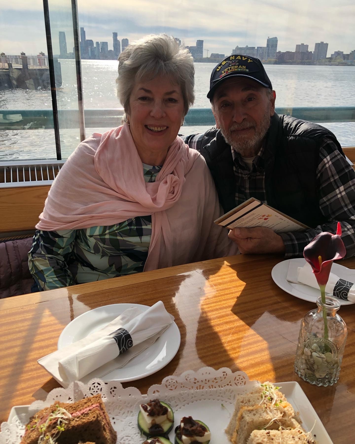 Smiling older couple at a table by the waterfront with city skyline.