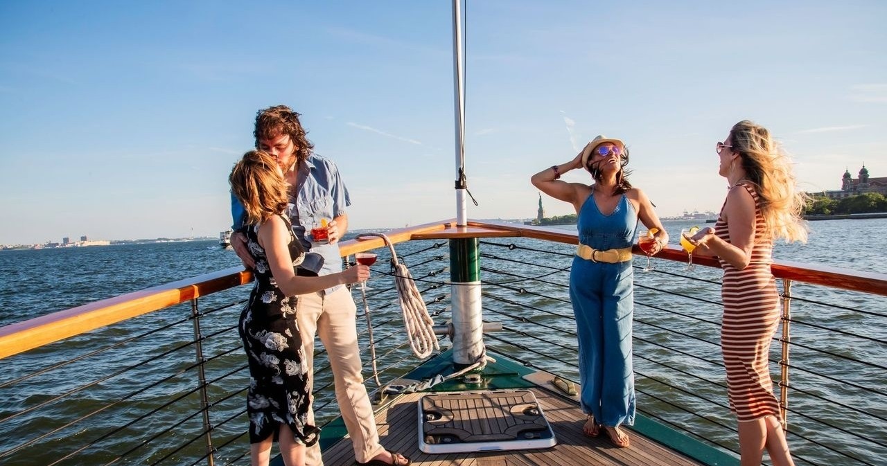 Four people on boat deck enjoying drinks with sea view.