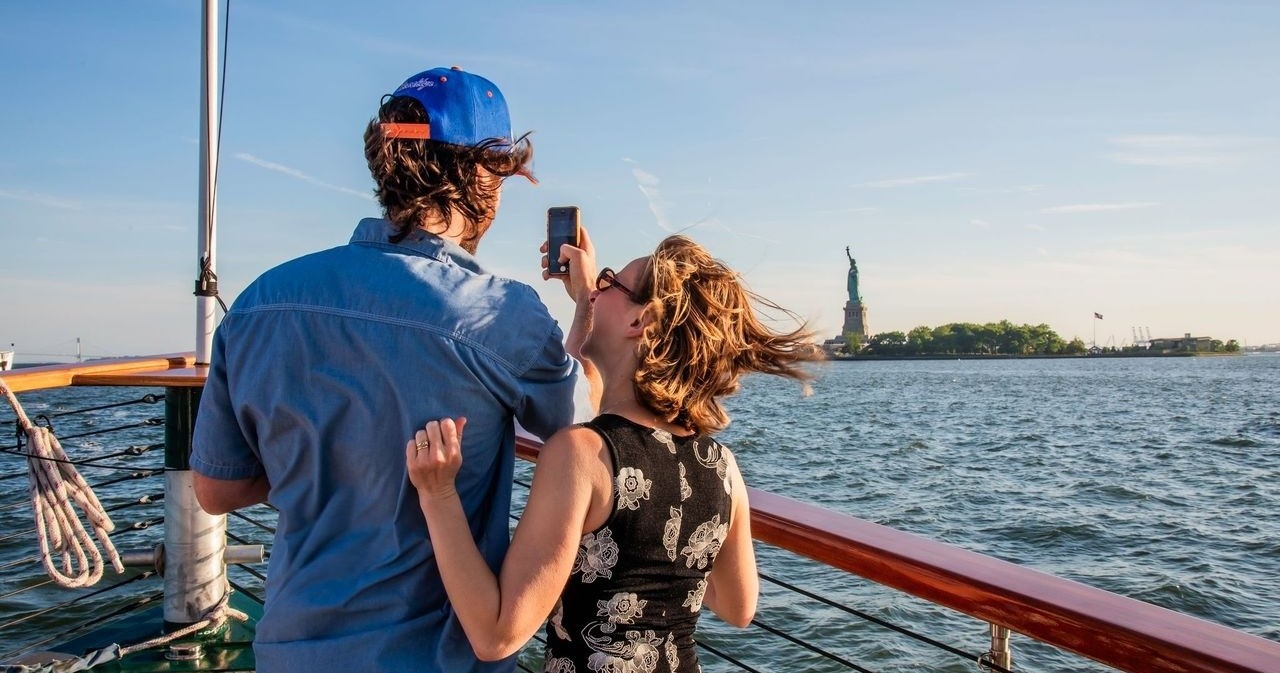 Two people on a boat, back to camera, with the Statue of Liberty in the background.