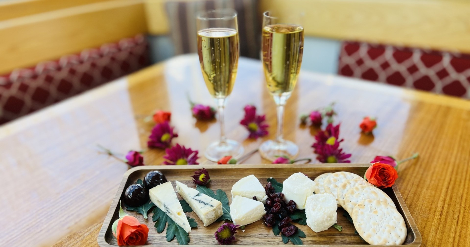 Two glasses of champagne with a cheese platter and flowers on a table.