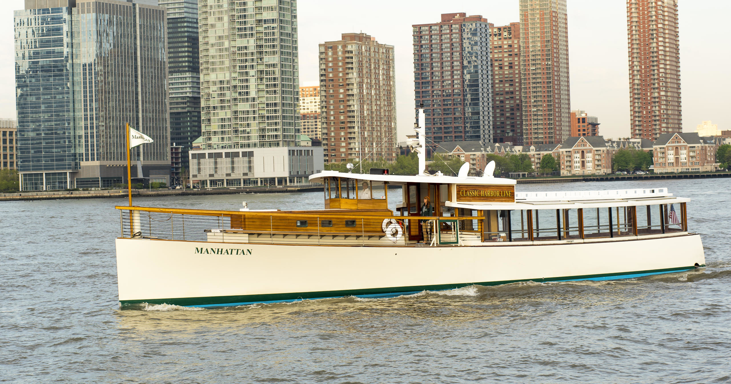 White boat sailing on a river with city skyline in the background.