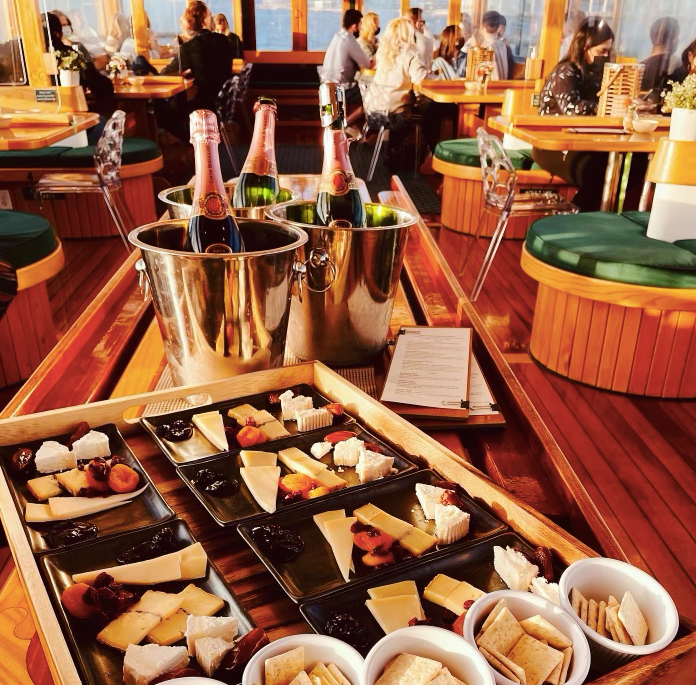 Cheese platters and champagne on a boat with seated guests.