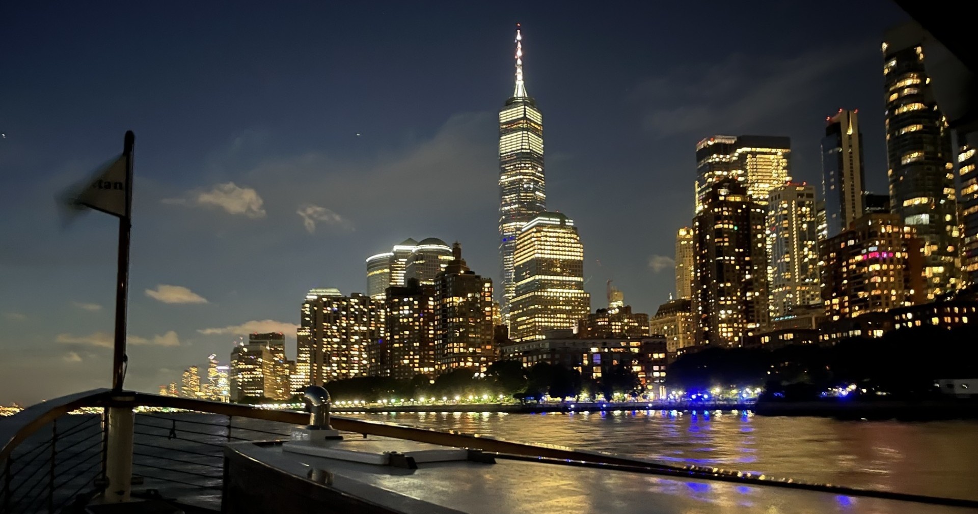 Night view of a city skyline with illuminated skyscrapers by a river.