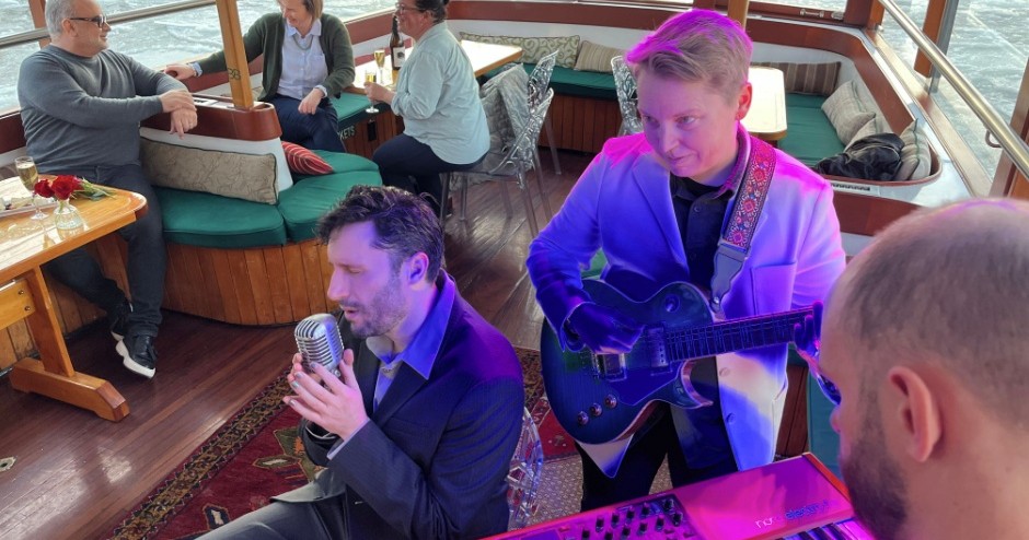 Musicians perform on a boat, with people sitting nearby.