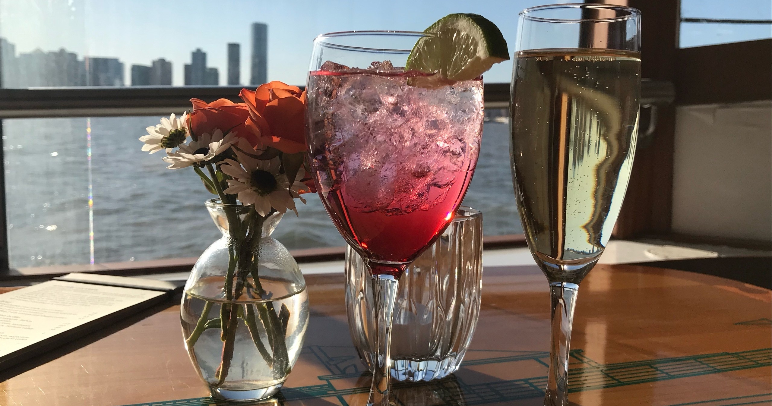 Drinks and flowers on a table with city skyline in background.