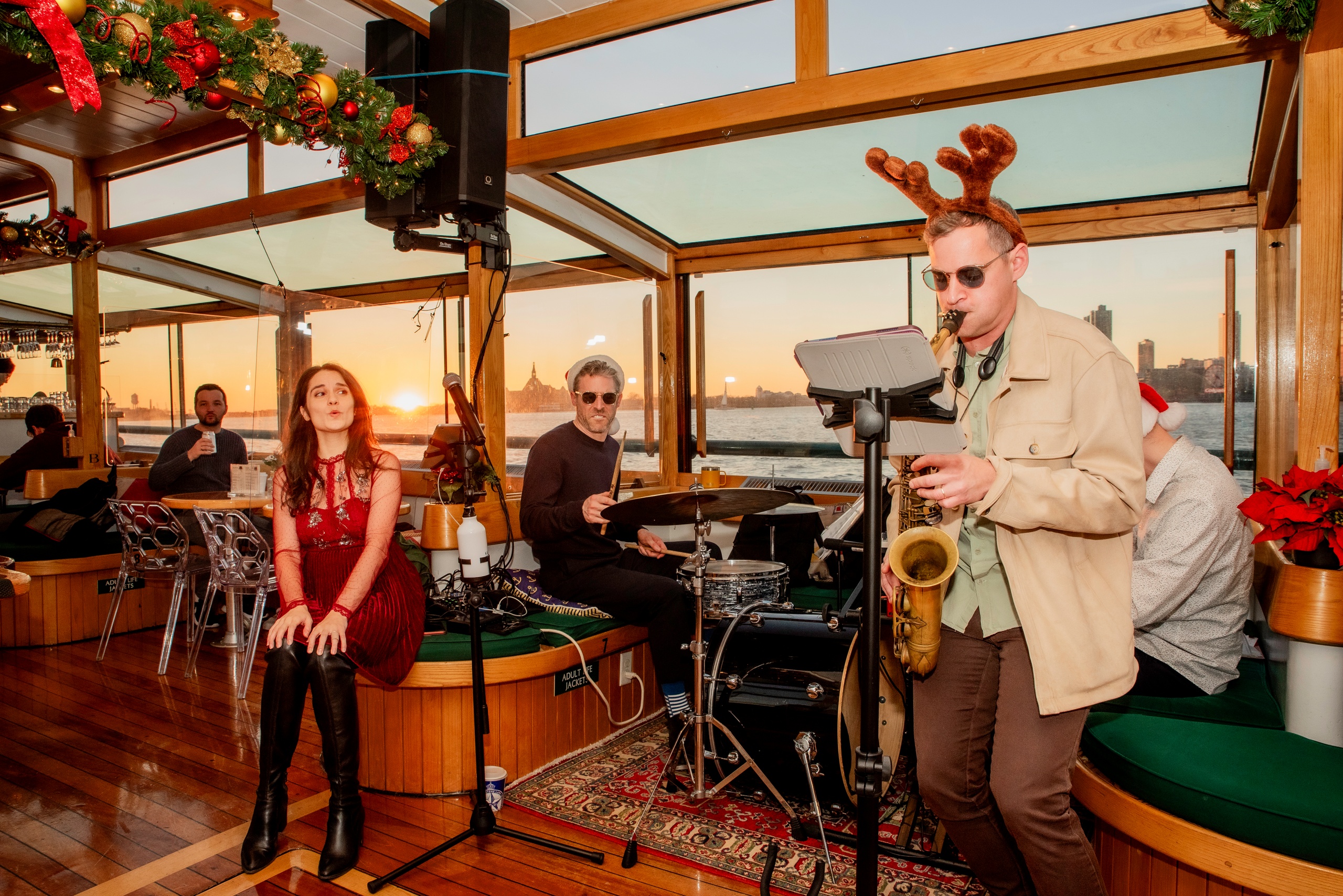 Musicians perform on a boat at sunset; saxophonist wears reindeer antlers.