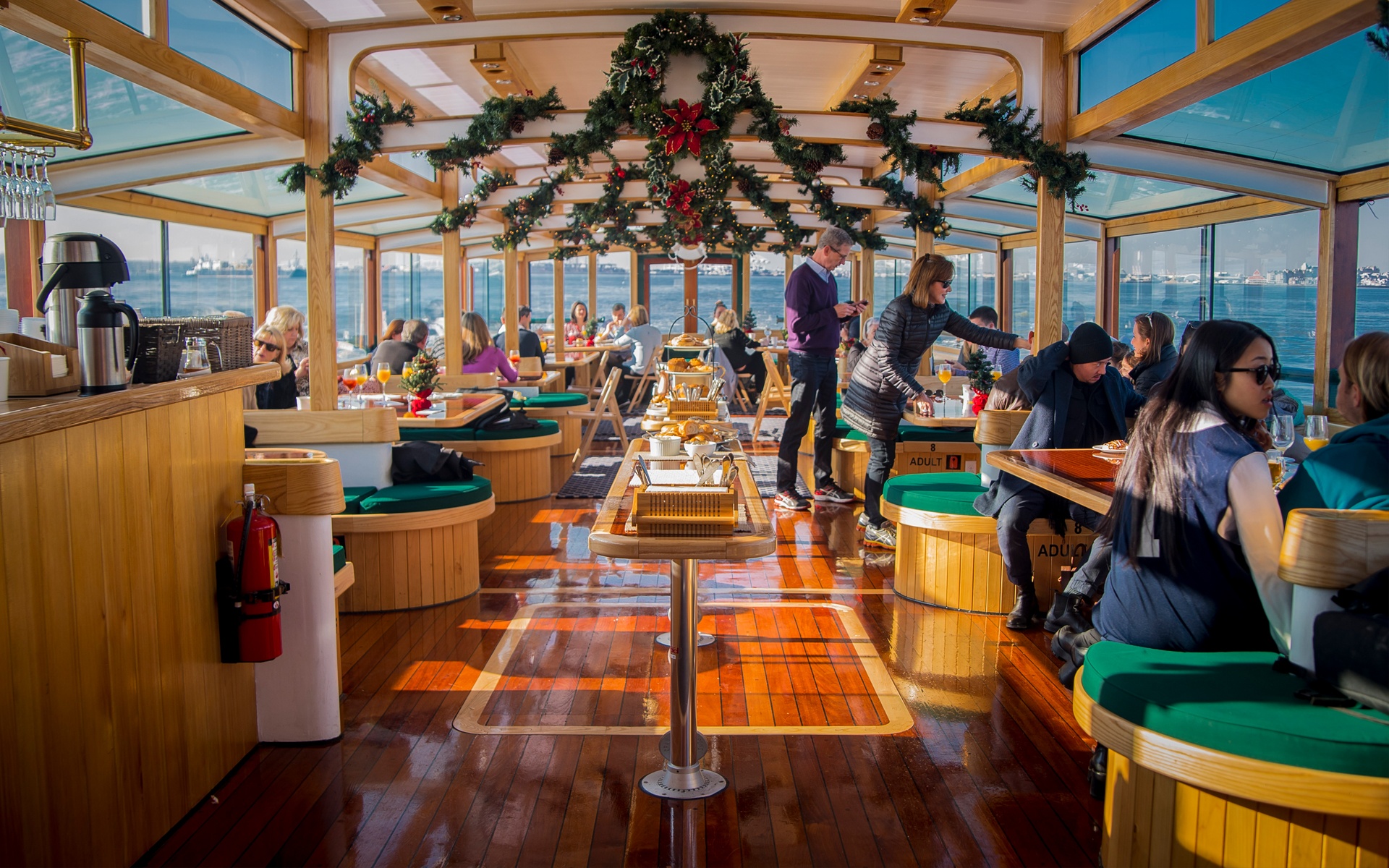People dining in a boat's festive interior with garlands and waterfront views.