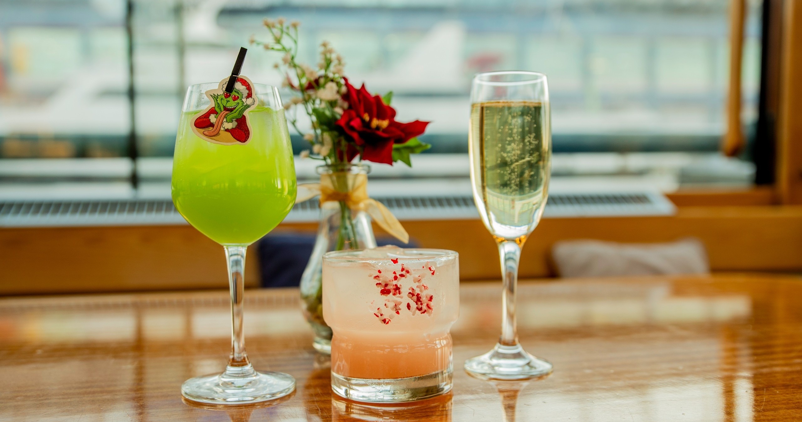 Three drinks: a green cocktail, a pink drink, and a filled champagne flute on a wooden table.