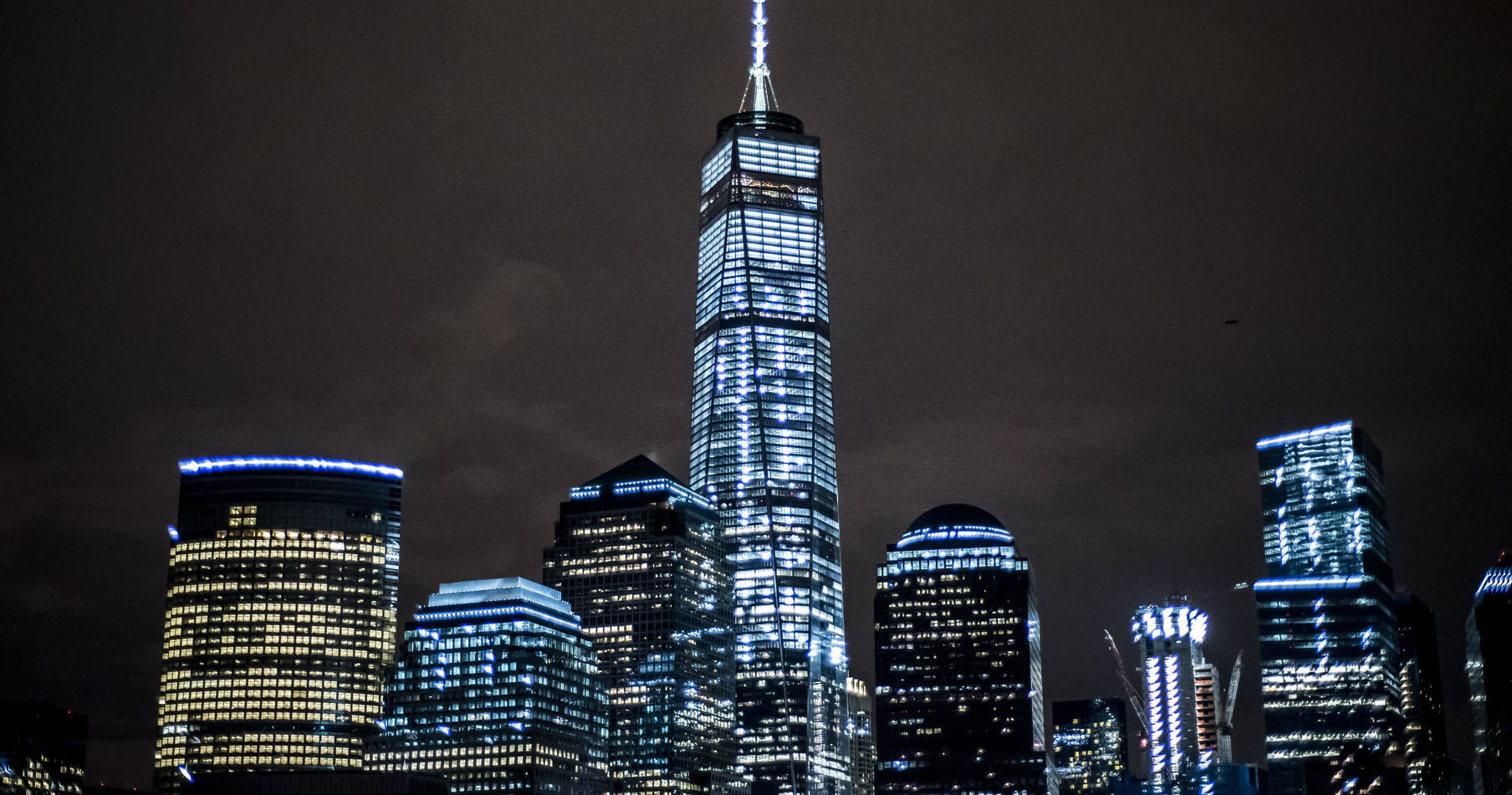 Night view of a city skyline with tall, illuminated skyscrapers and a dark sky.