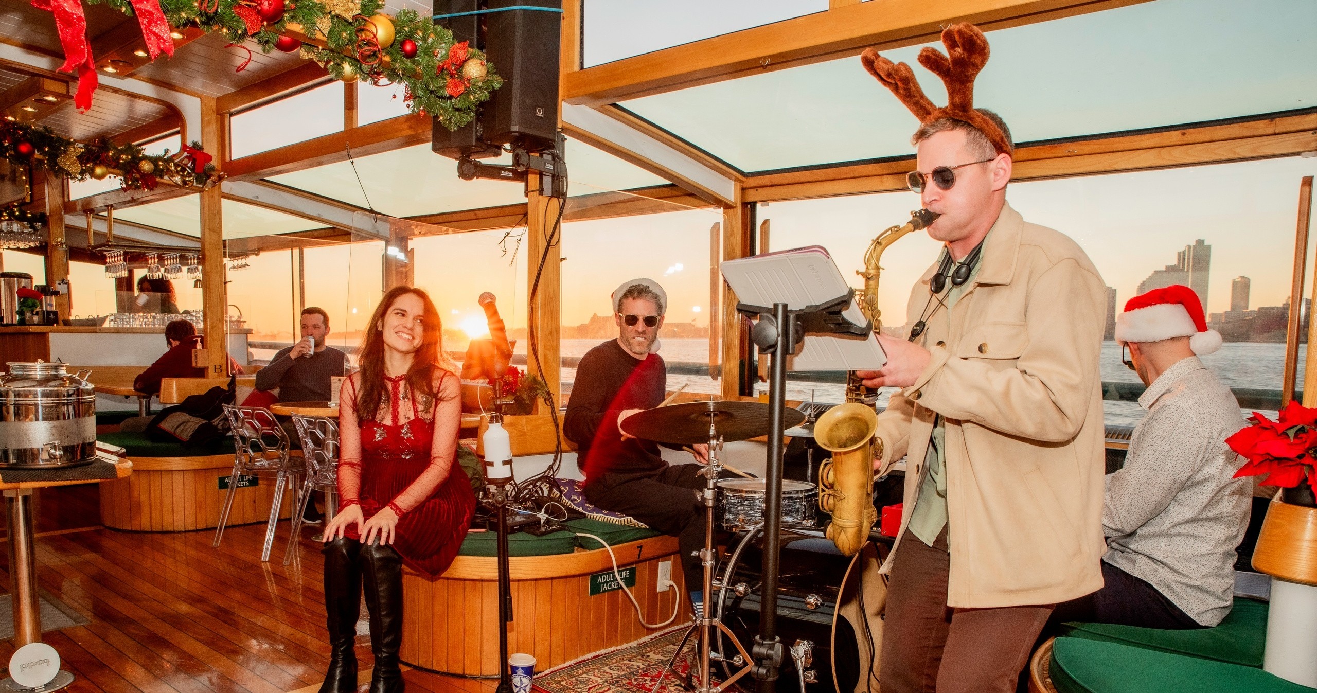 Musician with reindeer antlers plays saxophone on festive decorated boat.