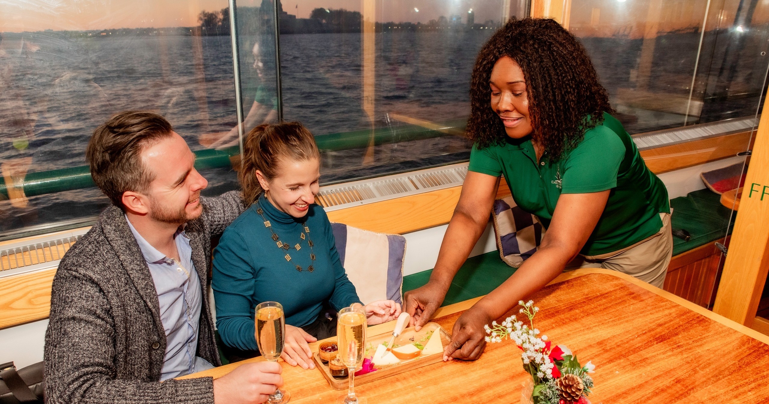Couple dining on a boat as a waitress serves them food.