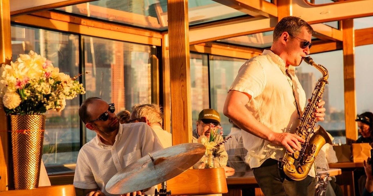 Musicians on a boat play saxophone and drums, with flowers nearby.