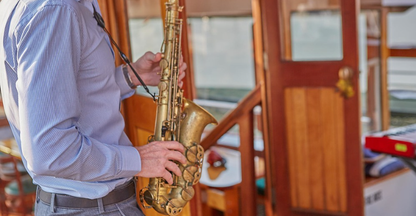 Person in striped shirt playing saxophone on a boat.